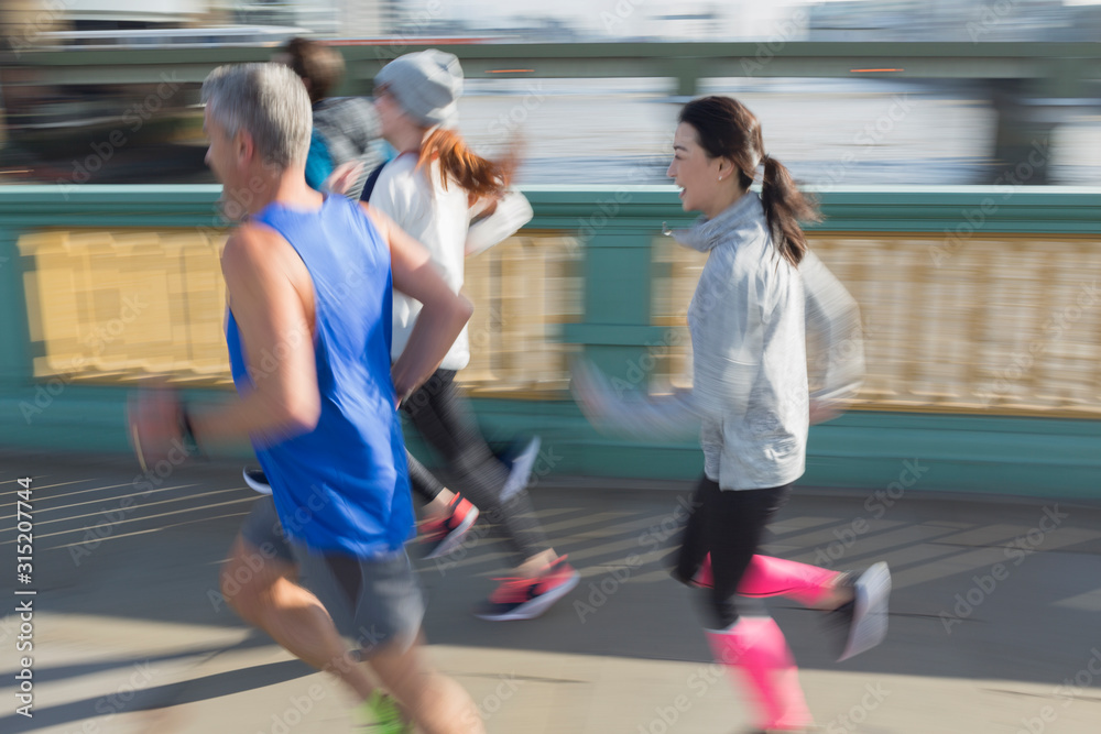 Runners running on sunny urban bridge sidewalk