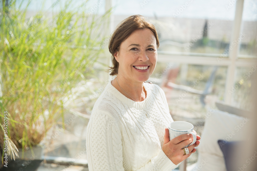 Portrait smiling mature woman drinking coffee in sunny sunroom Portrait smiling mature woman drinking coffee in sunny sunroom