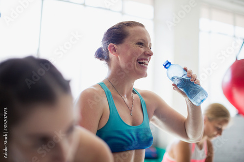 Laughing woman drinking water and resting post workout at gym photo