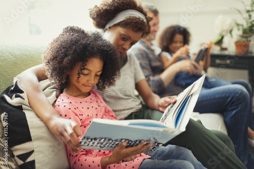 Parents reading books with daughters on living room sofa