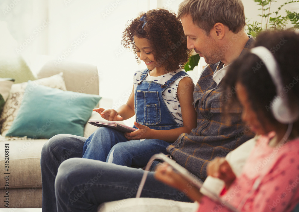 Multi-ethnic father and daughter using digital tablet on sofa Multi-ethnic father and daughter using digital tablet on sofa