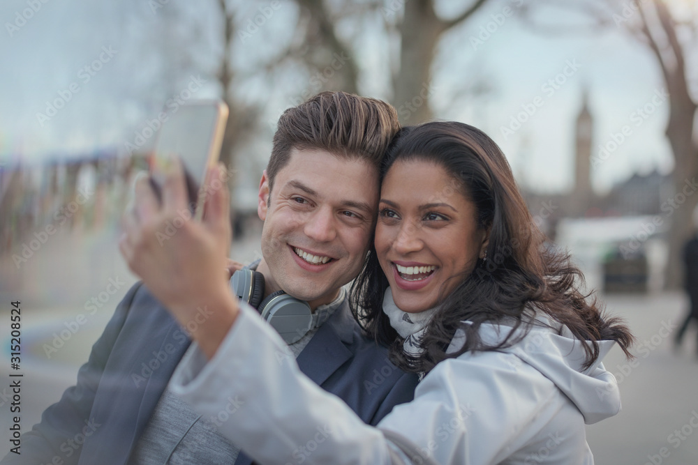 Smiling couple taking selfie with camera phone in urban park Smiling couple taking selfie with camera phone in urban park