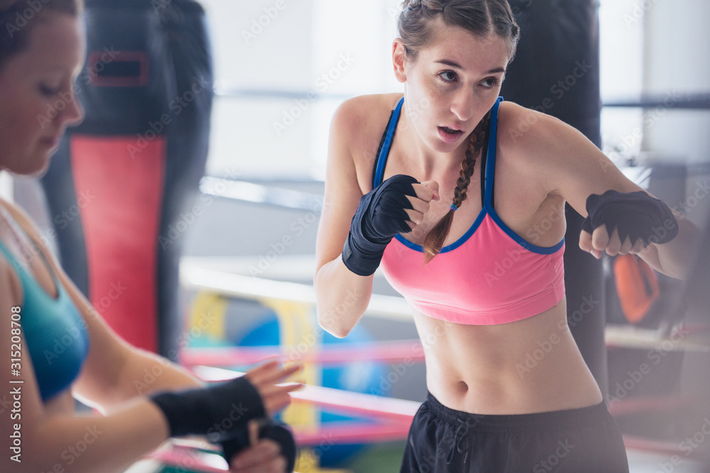 Determined, tough young female boxer shadowboxing in gym Determined, tough young female boxer shadowboxing in gym