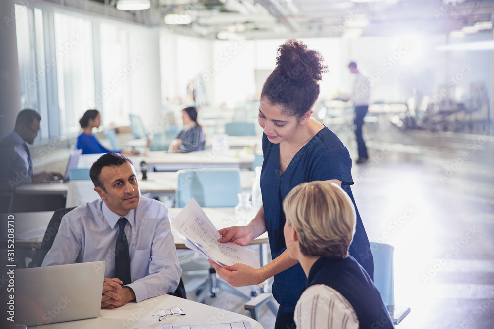 Businesswoman discussing paperwork with colleagues in office meeting Businesswoman discussing paperwork with colleagues in office meeting
