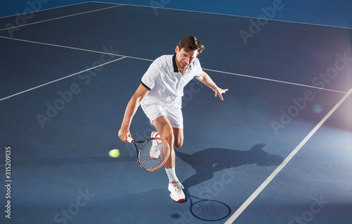 Young male tennis player playing tennis, reaching tennis racket on blue tennis court