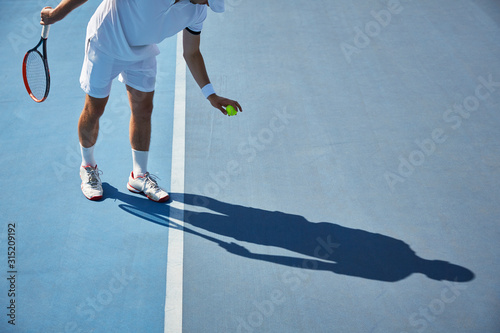 Young male tennis player playing tennis, bouncing tennis ball on sunny blue tennis court
