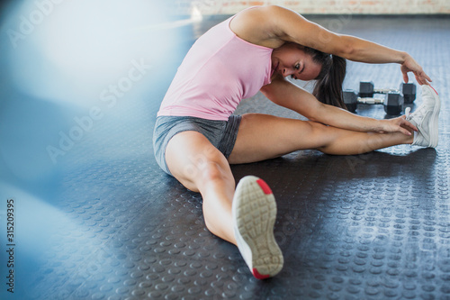 Young woman stretching leg and side in gym