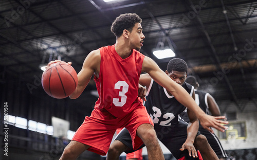 Young male basketball player dribbling the ball, playing game in gymnasium photo