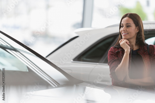 Smiling female customer eyeing new car in car dealership showroom