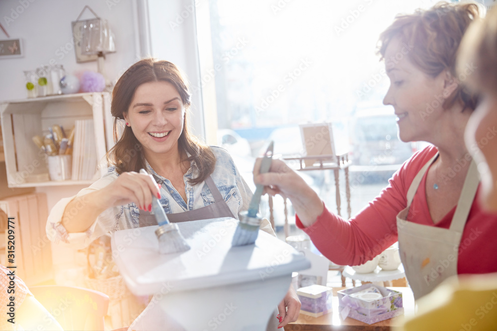 Smiling female artists painting bench blue in art class workshop Smiling female artists painting bench blue in art class workshop
