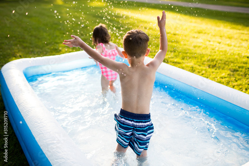 Preschool brother sister playing splashing in inflatable swimming pool photo