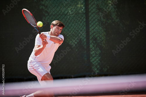 Young male tennis player playing tennis, hitting the ball on sunny tennis court