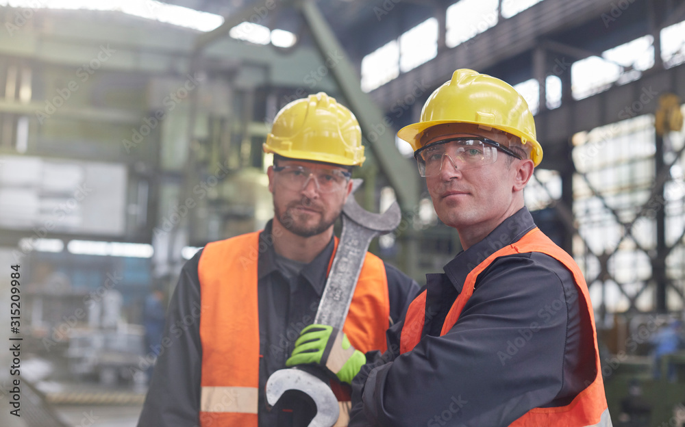 Portrait confident, tough male workers with large wrench in factory Portrait confident, tough male workers with large wrench in factory