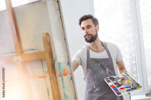 Male artist with palette painting at easel in art studio photo