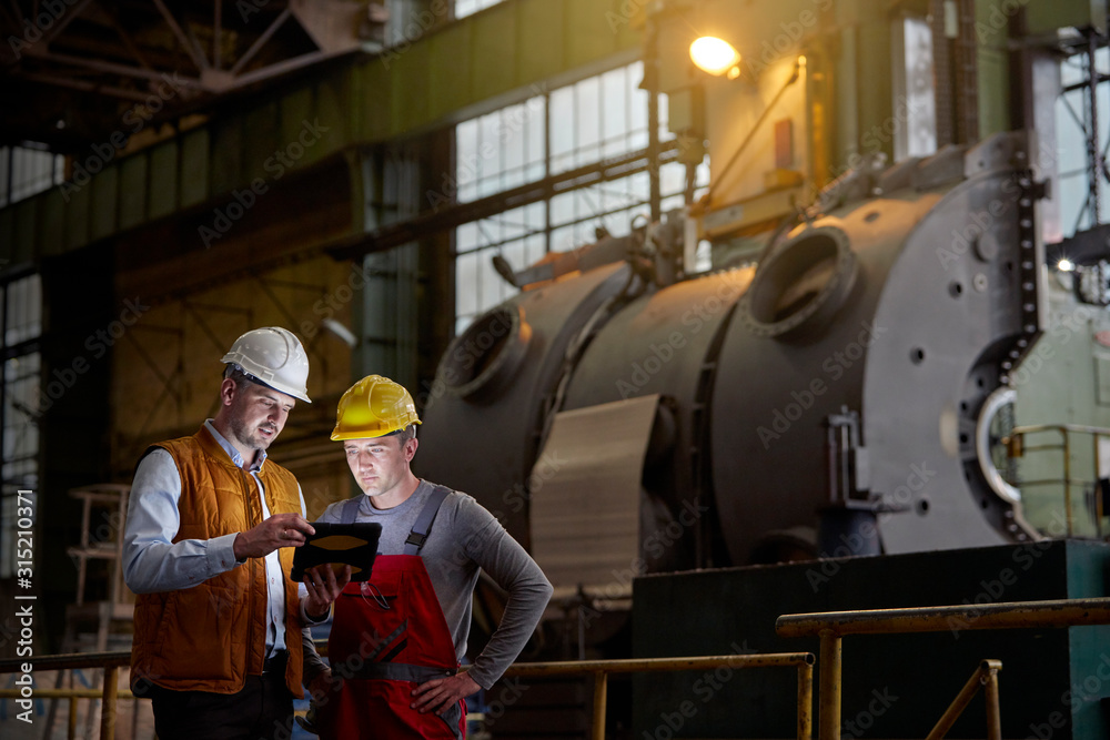 Male engineer and worker using digital tablet in dark factory Male engineer and worker using digital tablet in dark factory