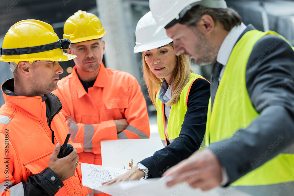 Engineers construction workers reviewing blueprints at construction site Engineers construction workers reviewing blueprints at construction site
