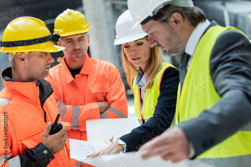 Engineers construction workers reviewing blueprints at construction site