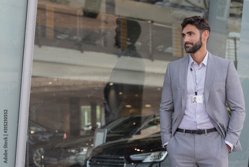 Portrait confident car salesman looking away outside car dealership showroom Portrait confident car salesman looking away outside car dealership showroom