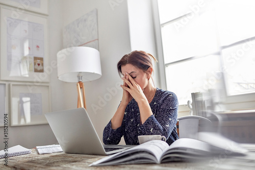 Tired, stressed businesswoman at laptop with head in hands