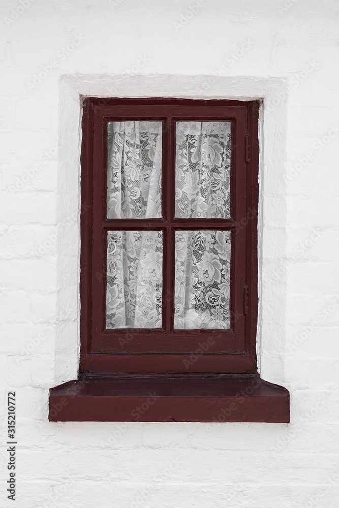 Obraz premium Generic old red wooden window frame against a white wall with delicate net curtains inside.