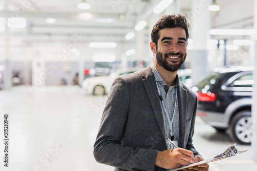 Portrait smiling, confident car salesman clipboard in car dealership auto repair shop