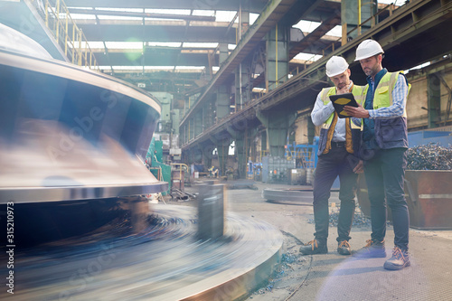 Male foreman and engineer with digital tablet talking in factory