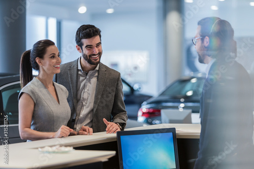 Couple customers talking to receptionist at desk in car dealership showroom photo