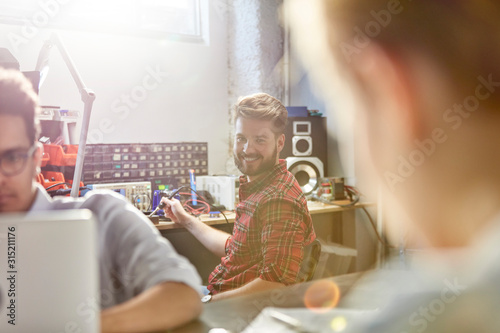 Portrait smiling engineer assembling electronics, using soldering iron in workshop