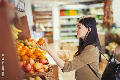Young woman shopping, examining oranges in grocery store