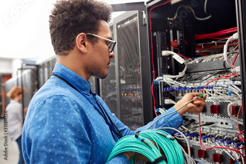 Male IT technician plugging cable into panel in server room photo
