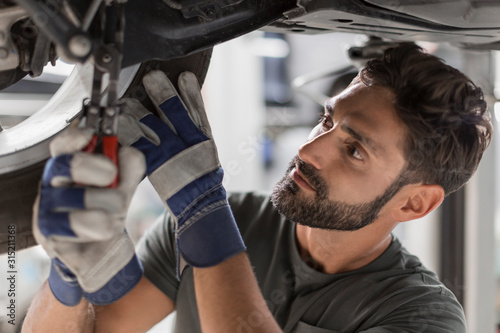 Focused male mechanic fixing wheel underneath car in auto repair shop photo