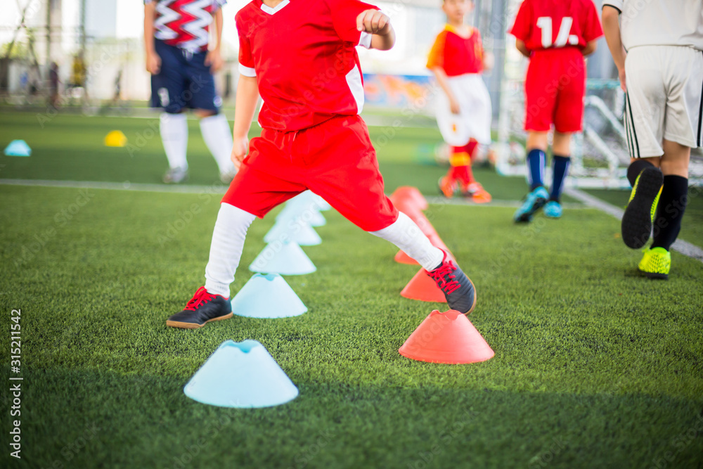 Kid soccer player Jogging and jump between red and blue cone markers on green artificial turf for soccer training. Football or soccer academy. Kid soccer player Jogging and jump between red and blue cone markers on green artificial turf for soccer training. Football or soccer academy.