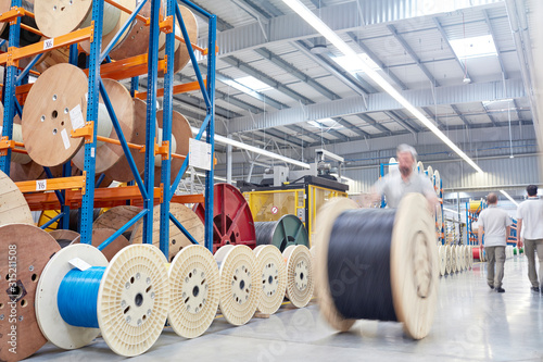 Male worker rolling large spool in fiber optics factory photo