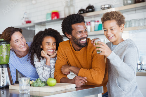 Multi-ethnic family making and drinking healthy green smoothie in kitchen photo
