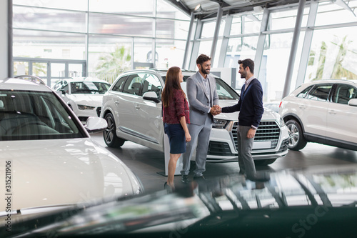Car salesman and customers handshaking in car dealership showroom