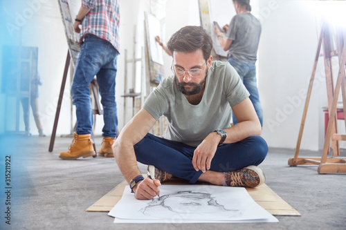 Male artist sitting cross-legged sketching on floor in art class studio