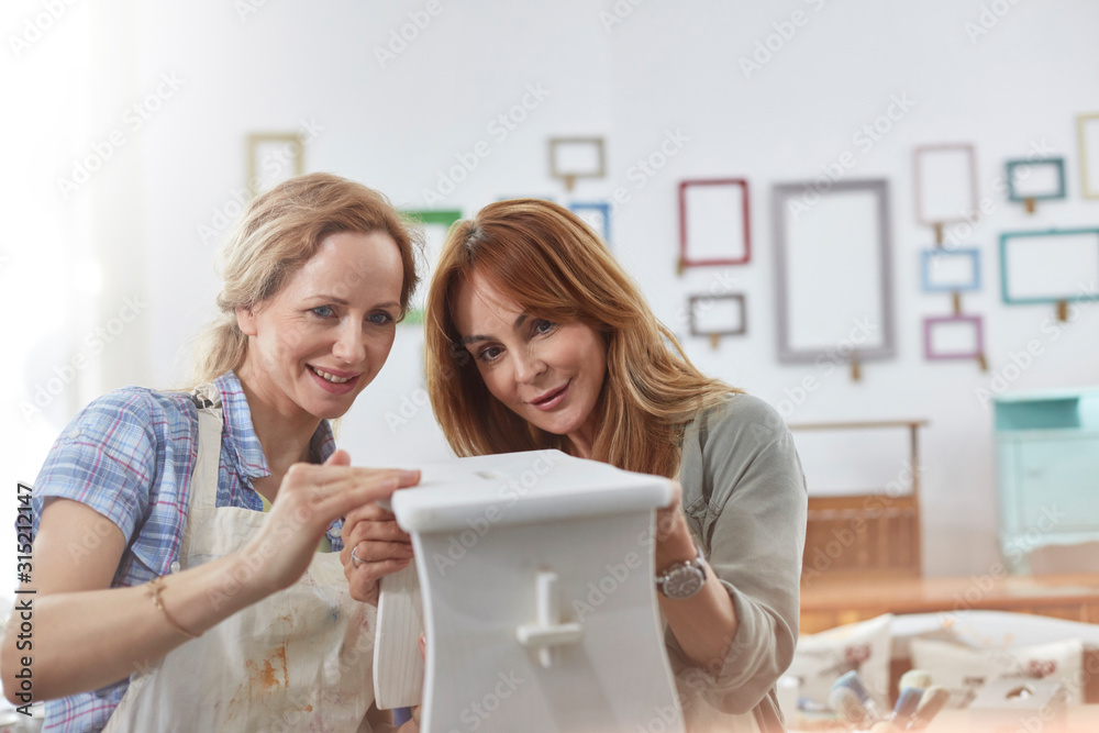 © Rafal Rodzoch/Caia Image - Female artists painting wooden bench in art class workshop