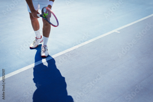 Young male tennis player preparing to serve the ball on sunny blue tennis court