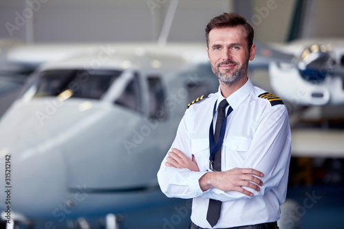 Portrait confident male pilot standing near airplane in hangar photo