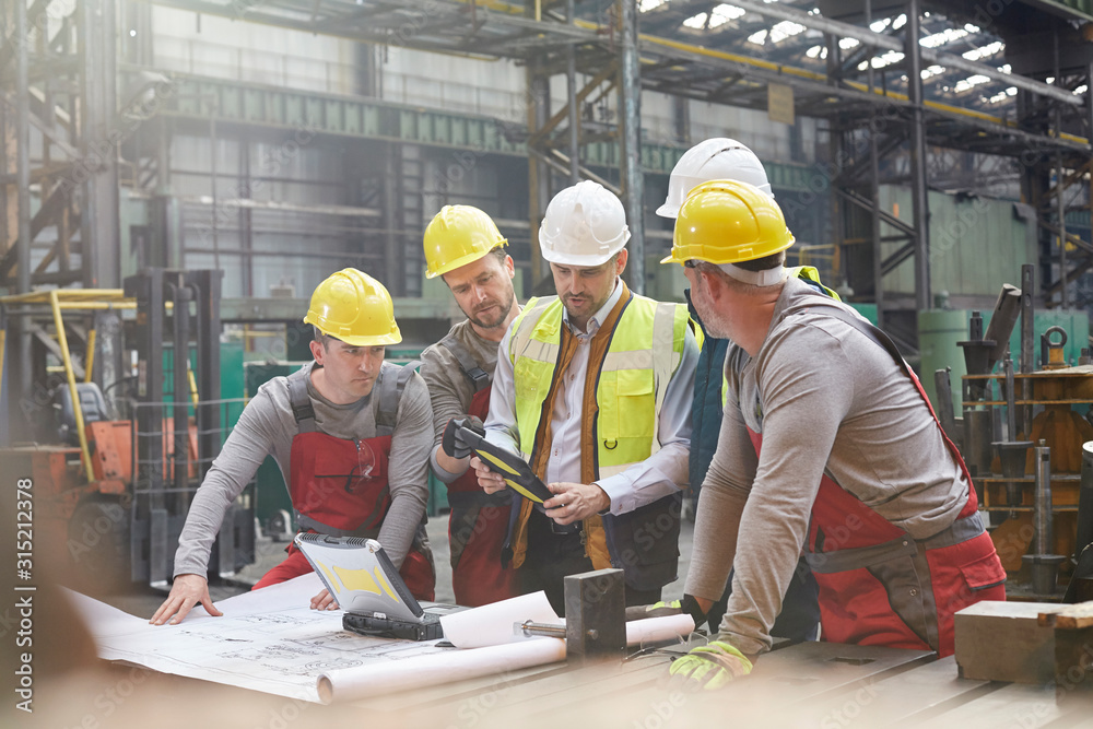 © Rafal Rodzoch/Caia Image - Male foreman, engineers workers with digital tablet meeting in factory
