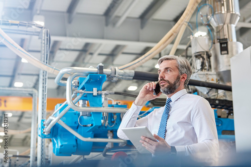 Male supervisor with digital tablet talking on cell phone in factory photo