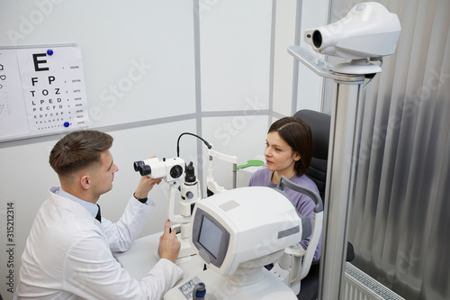 High angle portrait of male ophthalmologist using ophtalmic refractometer during consultation with female patient in clinic  copy space