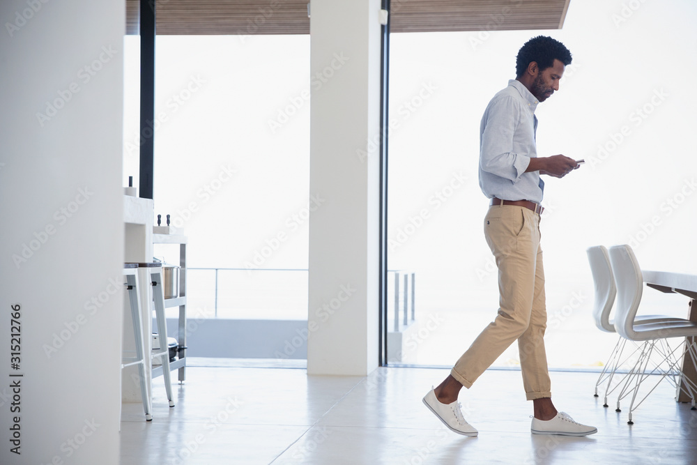 Businessman texting, walking in dining room Businessman texting, walking in dining room
