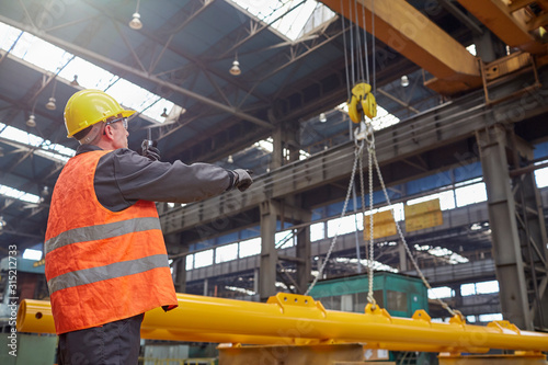 Male worker guiding hydraulic crane in factory photo
