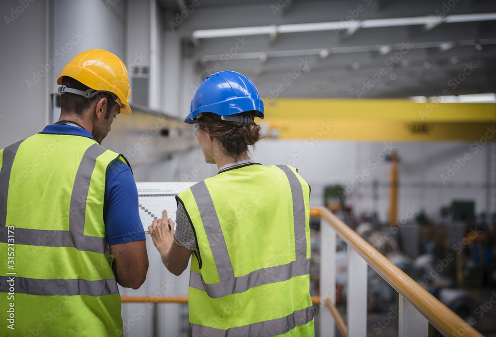 Supervisors discussing paperwork on platform in factory Supervisors discussing paperwork on platform in factory