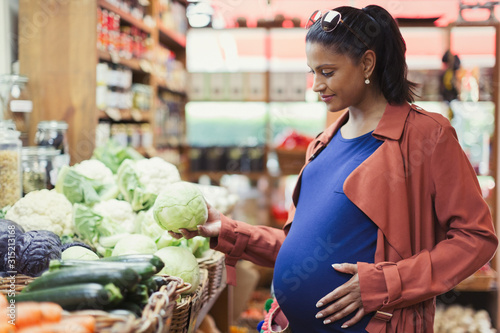 Pregnant woman shopping for cabbage in grocery store photo