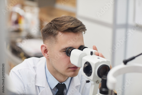 Closeup portrait of male optometrist using refractometer machine while testing vision of unrecognizable patient