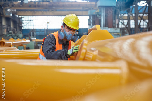 Steel worker wearing protective face mask, examining equipment in steel factory