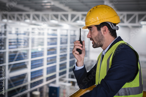 Male supervisor talking, using walkie-talkie on platform in factory