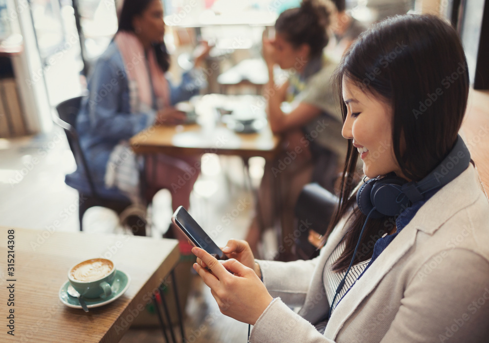 © Caiaimage/Paul Bradbury/Caia Image - Smiling young woman texting cell phone drinking coffee at cafe table